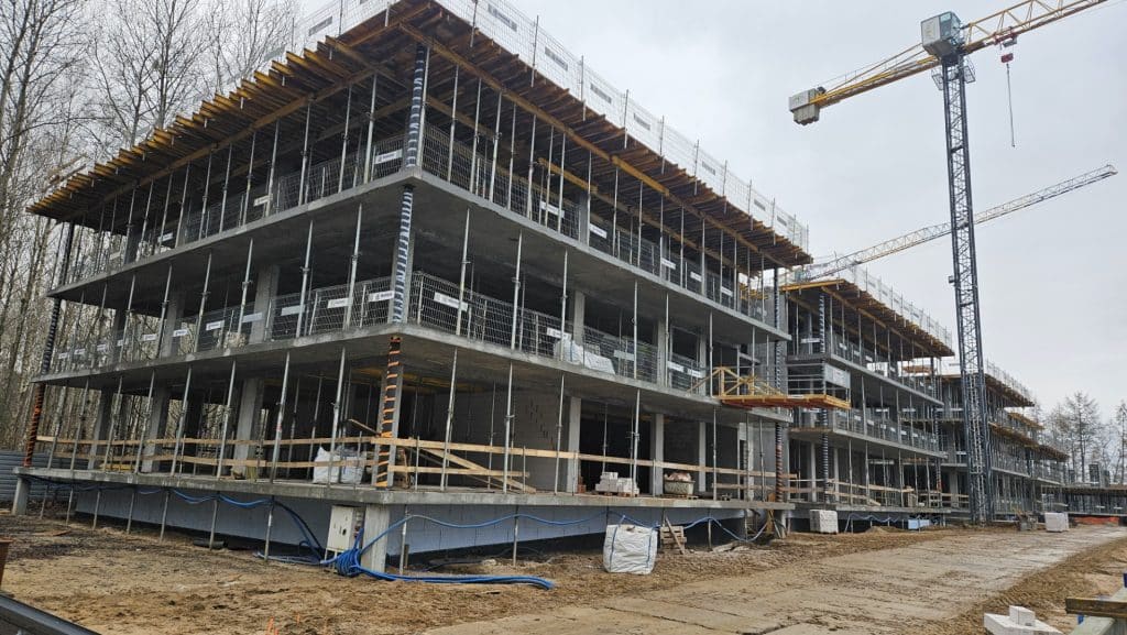 Budowa nowego budynku przy jeziorze Ukiel w Olsztynie, wok&oacute;ł teren budowy i maszyny budowlane.