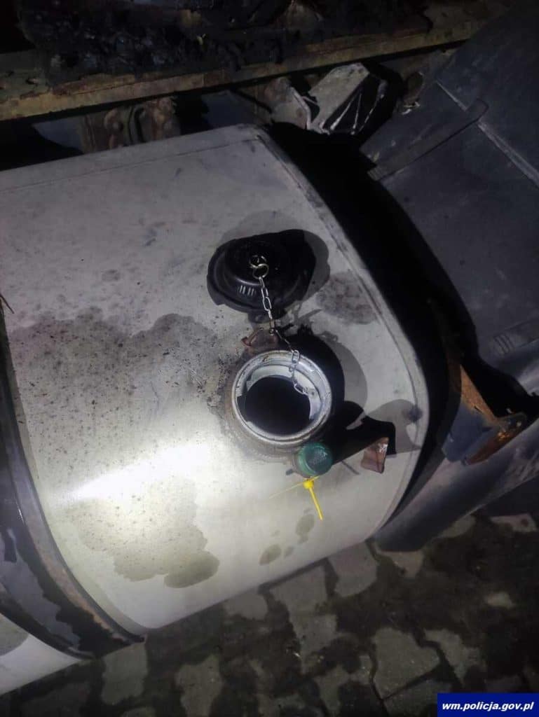 Widok na zbiornik paliwa samochodu z otwartym korkiem i zabezpieczeniem, nocą, na parkingu.