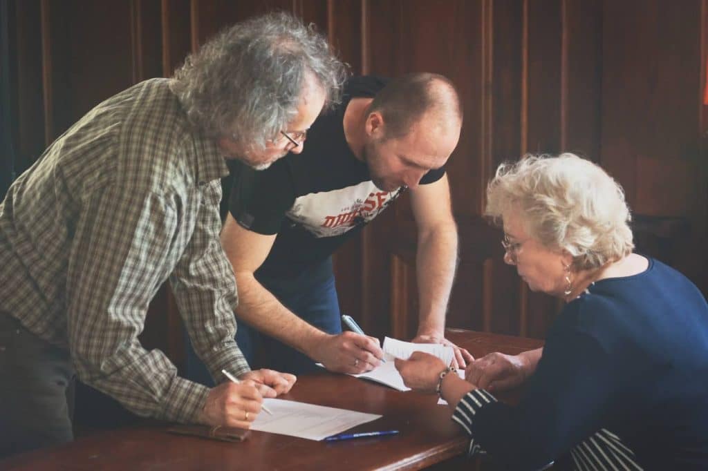 Trzy osoby podpisują dokumenty podczas spotkania organizacji społecznych w Olsztynie.