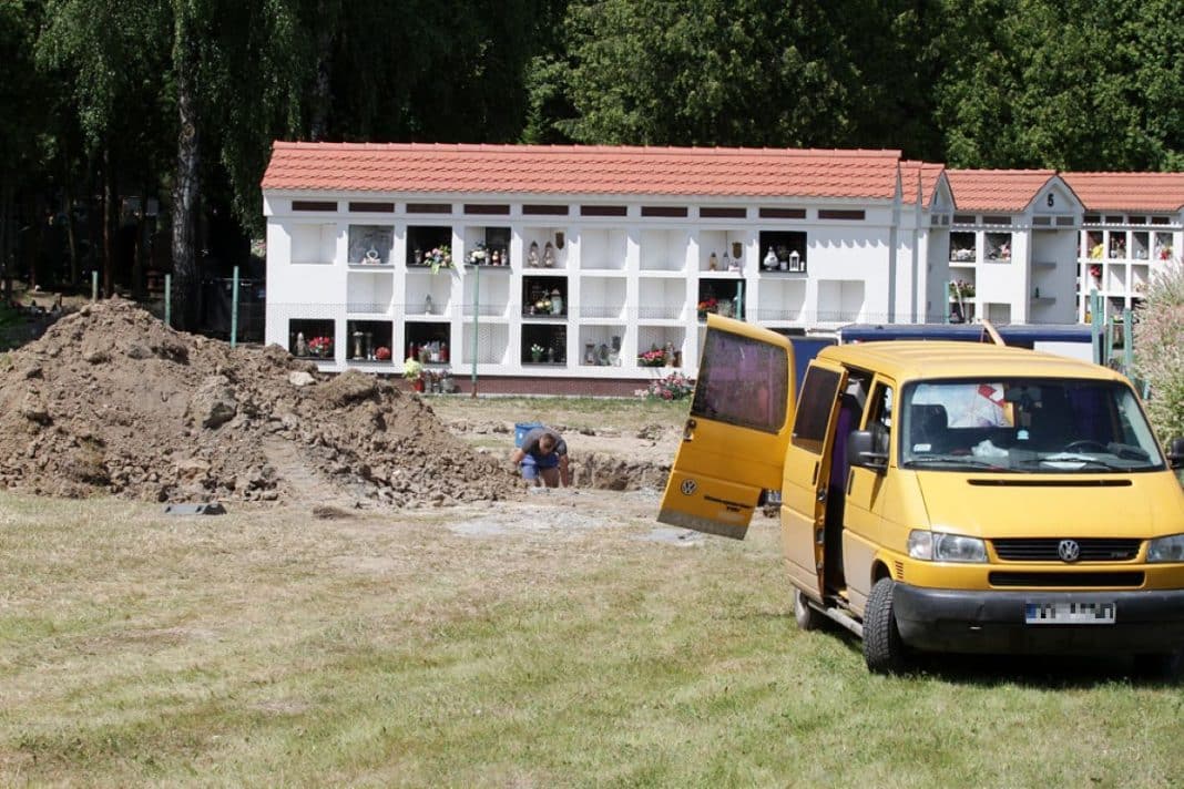 Prace budowlane na cmentarzu przy ul. Poprzecznej, w tle kolumbarium z grobami i samoch&oacute;d dostawczy.