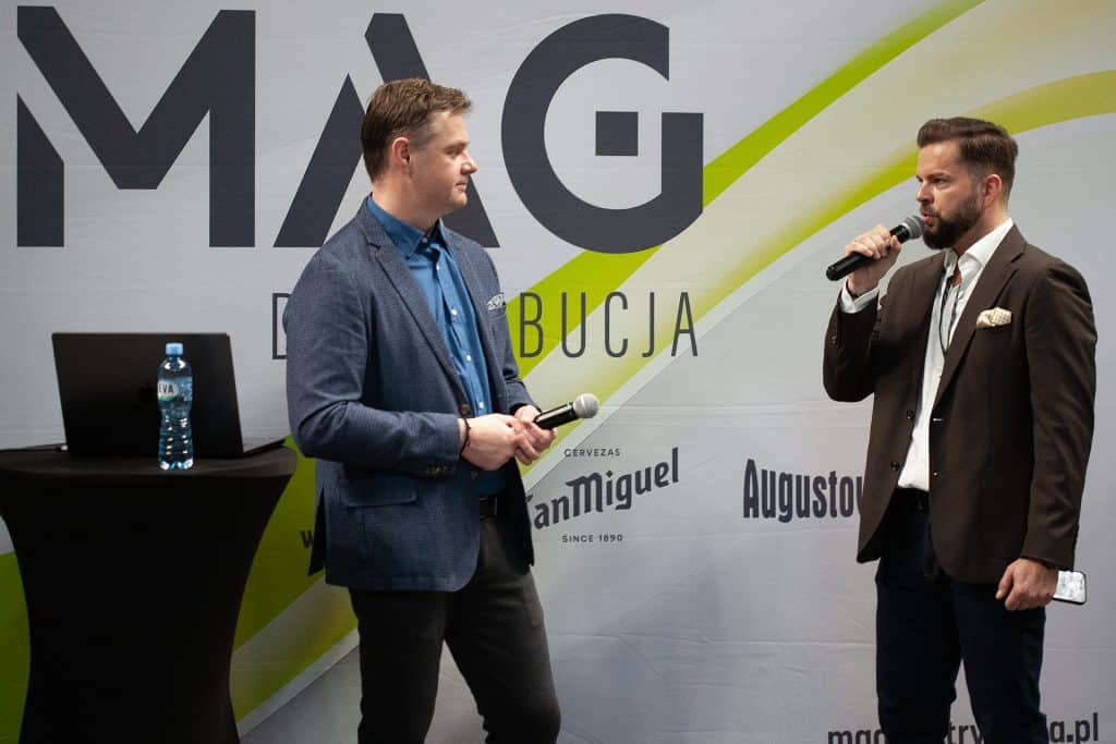 Dw&oacute;ch mężczyzn rozmawia na scenie podczas targ&oacute;w branżowych w Olsztynie, za nimi logo wydarzenia.