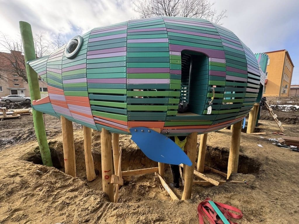 Kolorowa konstrukcja przypominająca rybę na placu budowy w Giżycku.