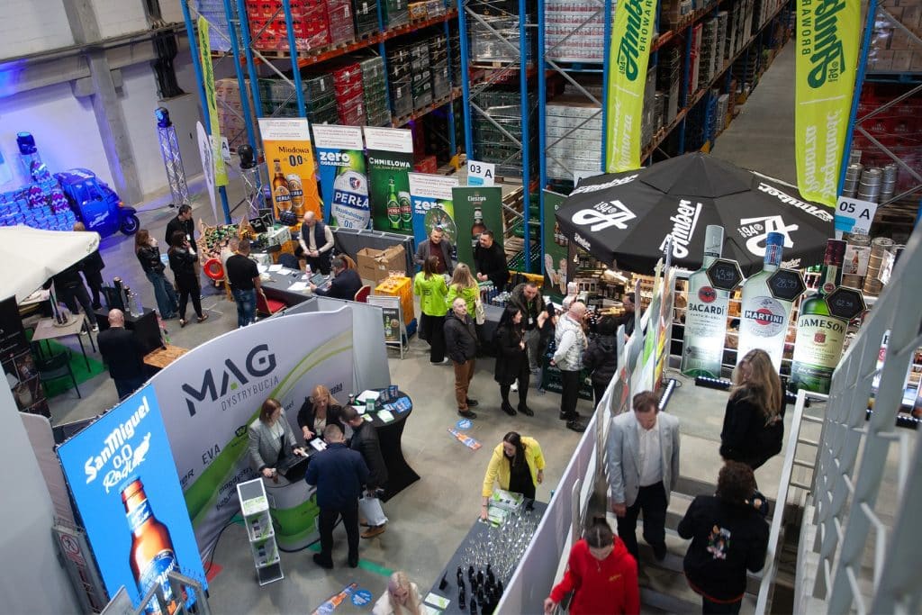 Targi biznesowe w Gdańsku z wystawcami, stoiskami i uczestnikami w hali magazynowej.