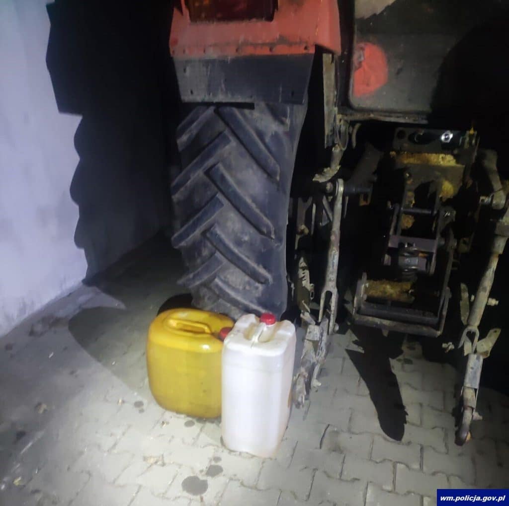 Teren firmy w nocy, widoczny traktor i dwa kanistry na ziemi.