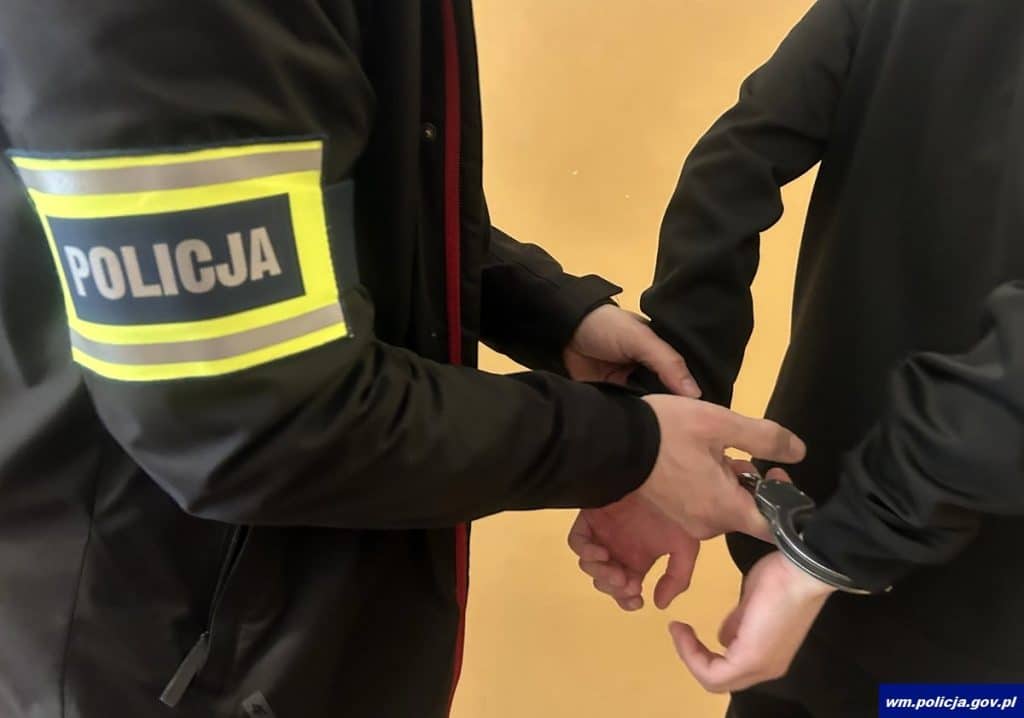 Policjant zatrzymuje osobę poszukiwaną, trzymając ją za ręce w trakcie akcji policyjnej.