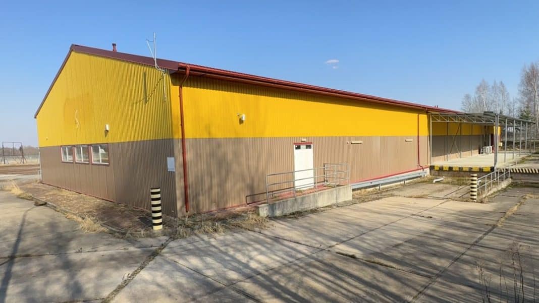 Opuszczony pawilon handlowy w Pierselach, zamknięty i wystawiony na sprzedaż, z ż&oacute;łto-brązową elewacją.