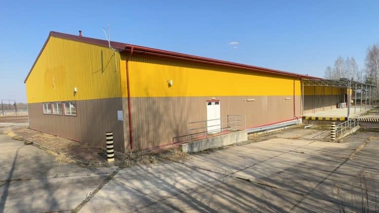 Opuszczony pawilon handlowy w Pierselach, zamknięty i wystawiony na sprzedaż, z ż&oacute;łto-brązową elewacją.