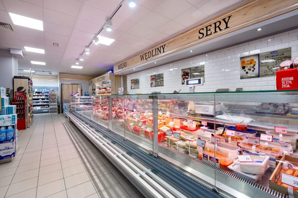 Wnętrze sklepu spożywczego z ladami z mięsem i wędlinami, oznaczone sekcje sezonowe.