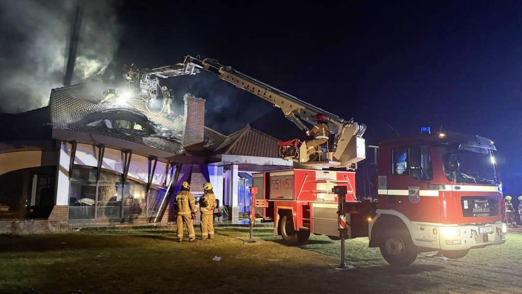 Strażacy gaszą pożar luksusowego domu na Mazurach w nocy, używając podnośnika i węży gaśniczych.