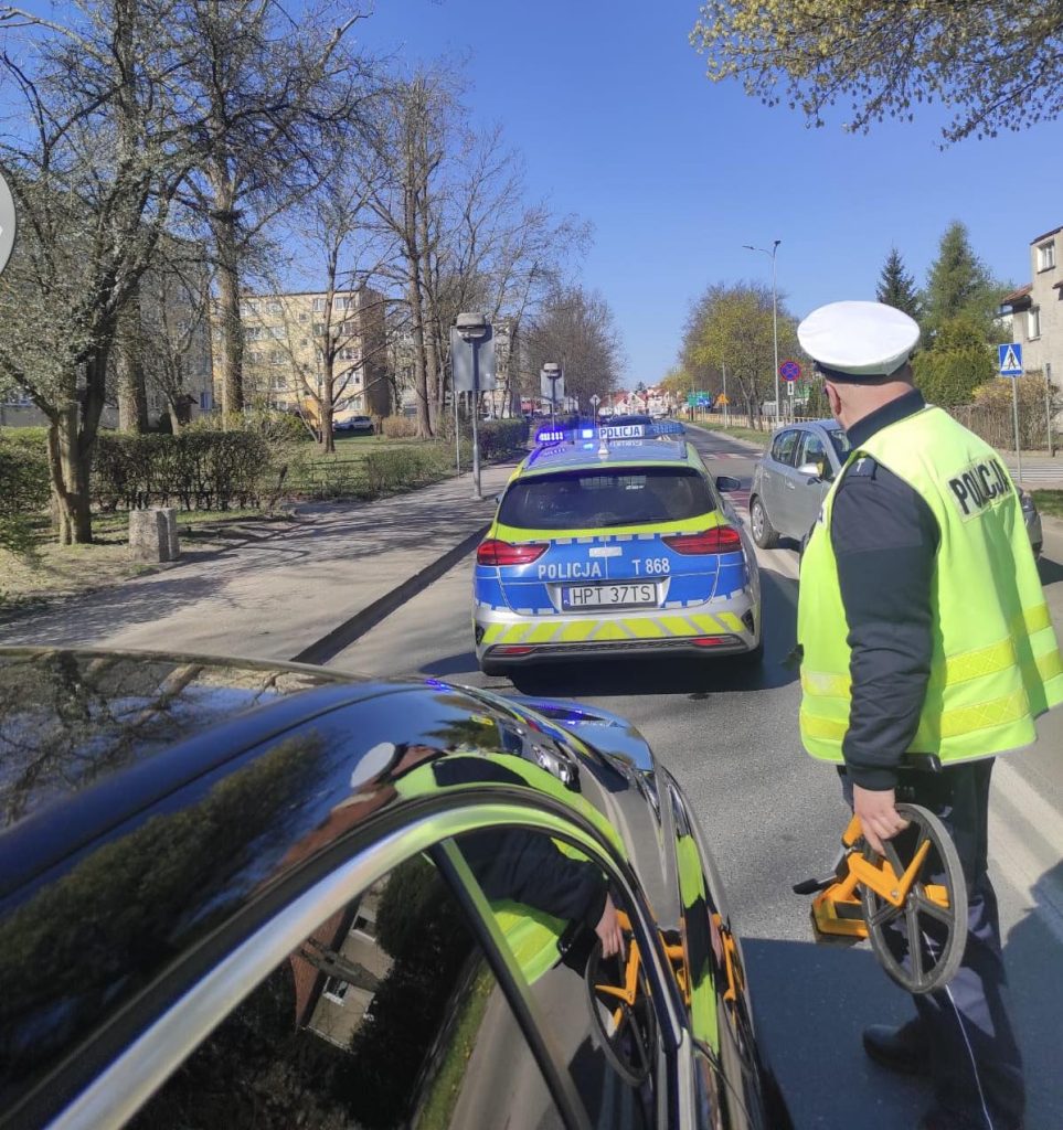 Policjant i radiow&oacute;z na miejscu wypadku na przejściu dla pieszych, w tle ulica i drzewa.