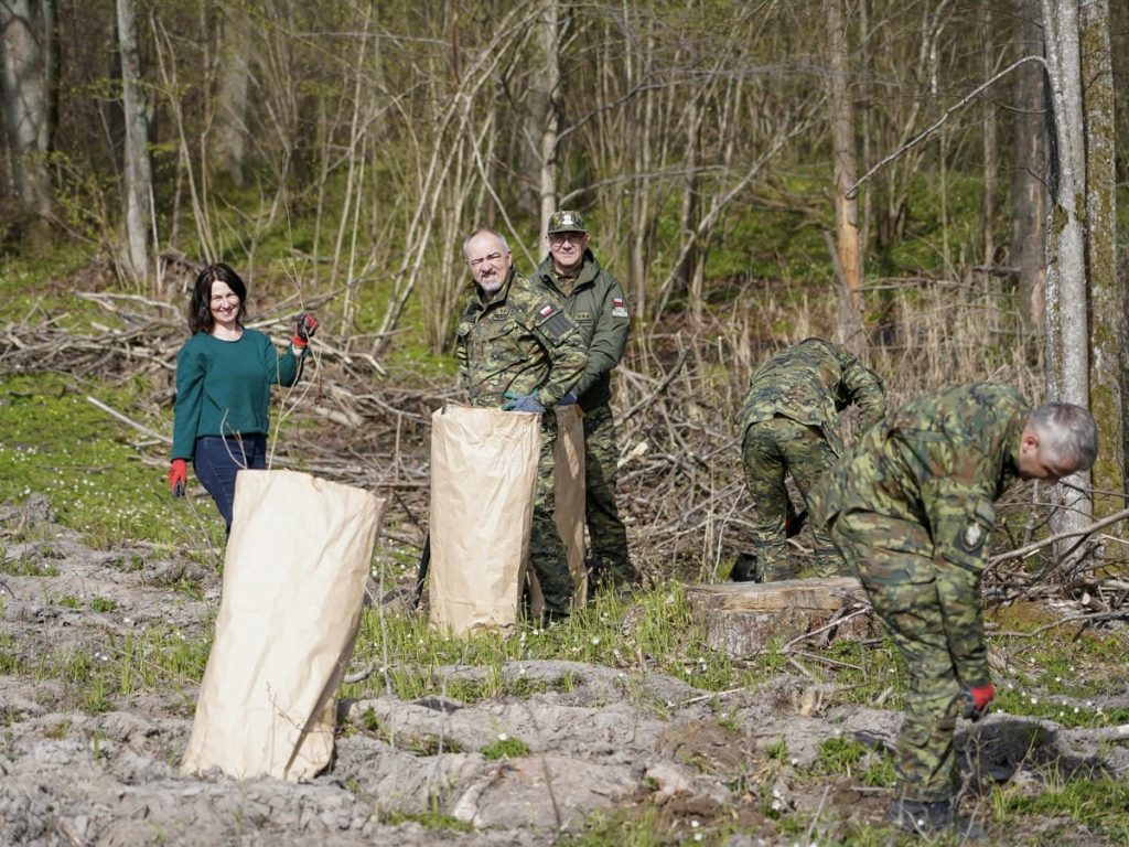 Grupa ludzi sadzi drzewa w lesie na Mazurach, wśr&oacute;d drzew i gałęzi, w ramach akcji ekologicznej.