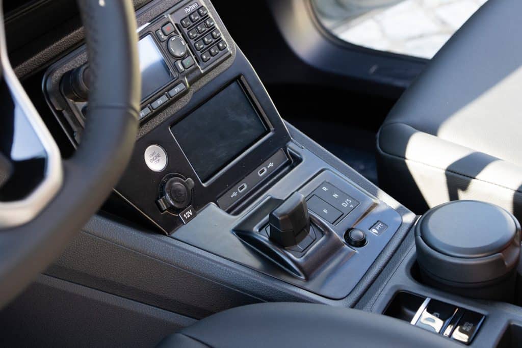 Wnętrze policyjnego samochodu z widocznym panelem sterowania i dźwignią zmiany bieg&oacute;w.