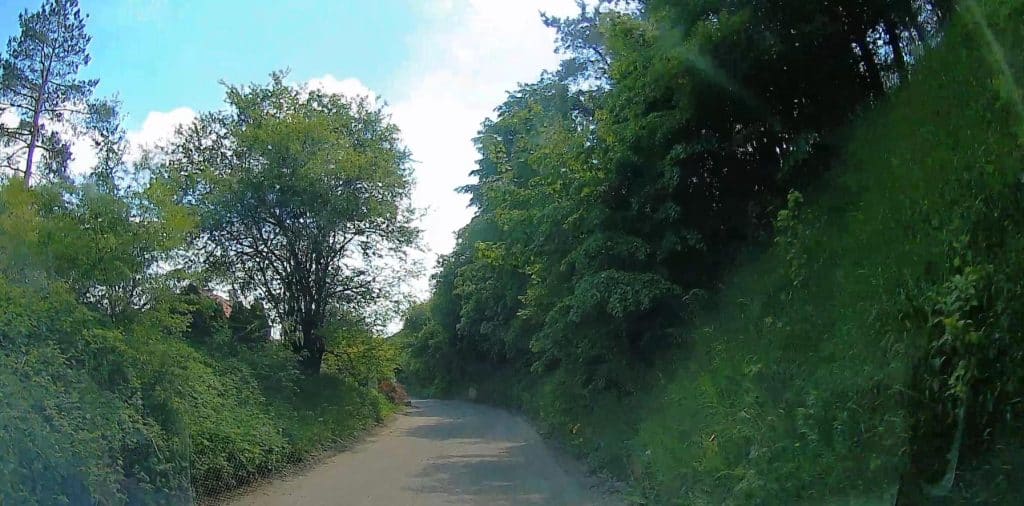 Wąska, nier&oacute;wna droga w otoczeniu zieleni, zakończona modernizacją.