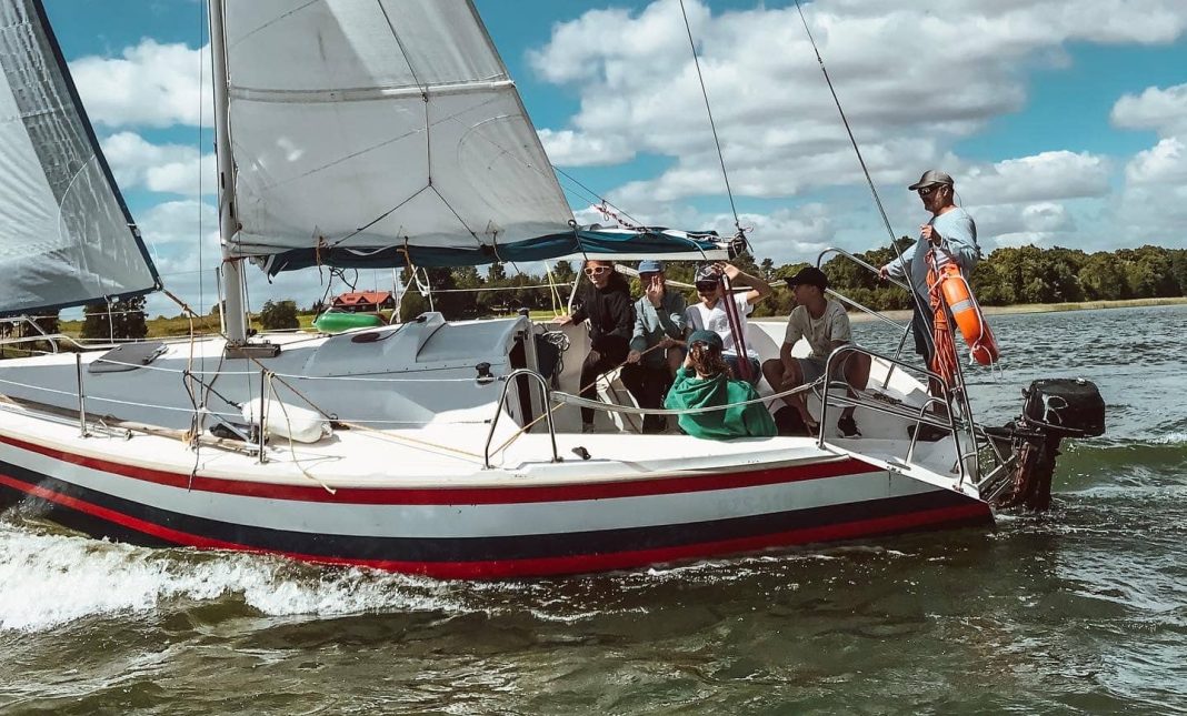 Grupa młodych ludzi na jachcie na jeziorze pod chmurami, aktywny wypoczynek na Mazurach.