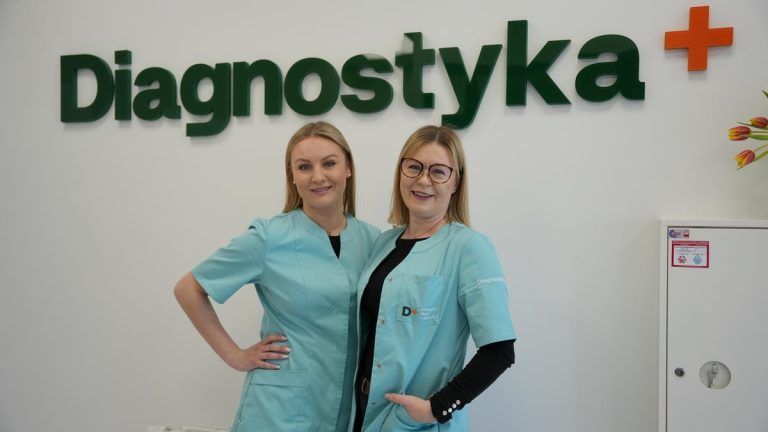 Dwie kobiety w uniformach medycznych stoją przed napisem 'Diagnostyka+' w nowym punkcie pobrań w Olsztynie.