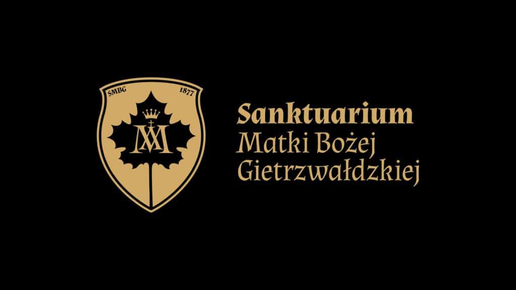 Herb sanktuarium z napisem, w kolorze złotym na czarnym tle, symbolizujący Gietrzwałd i jego religijne znaczenie.