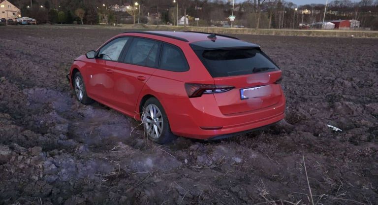 Czerwony samoch&oacute;d osobowy wjechał na pole po nieudanym manewrze na drodze.
