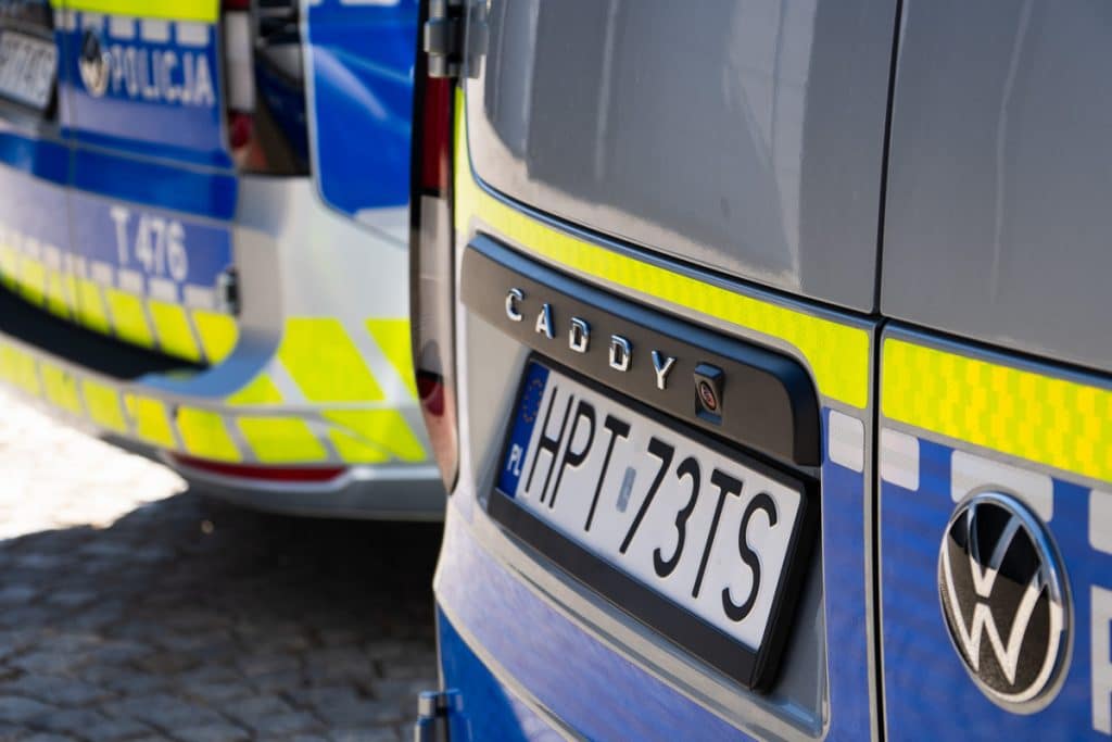 Zbliżenie na oznakowane policyjne radiowozy na Mazurach, widoczne numery rejestracyjne i logo VW.