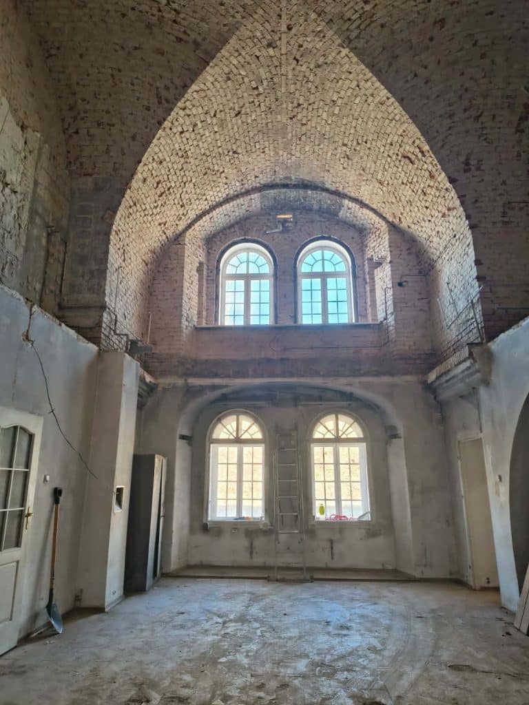 Wnętrze zabytkowej twierdzy z ceglaną architekturą i dużymi oknami, w trakcie remontu.