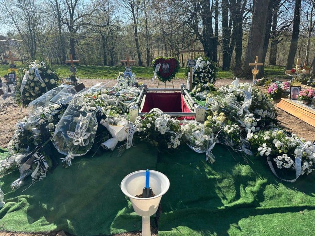 Gr&oacute;b chłopca ozdobiony kwiatami i wieńcami podczas pogrzebu w lesie.