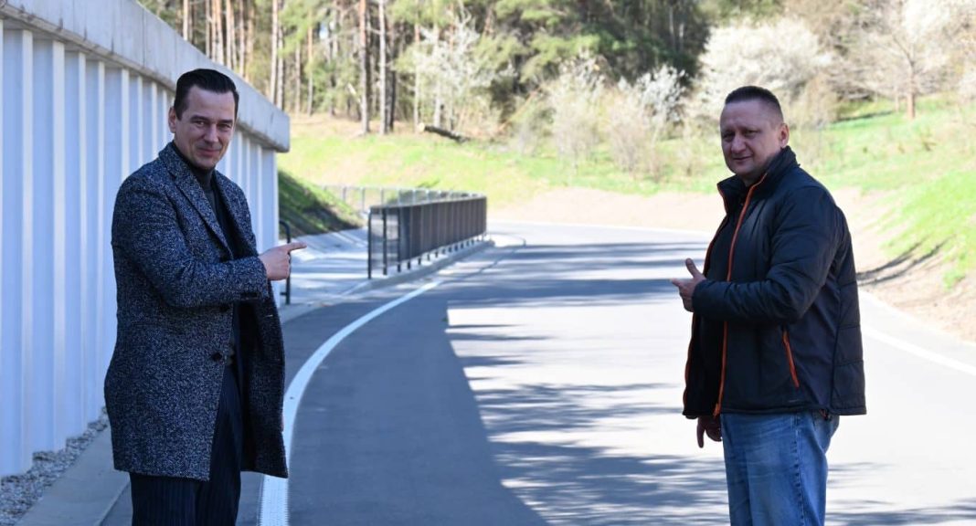 Dw&oacute;ch mężczyzn na nowo wybudowanej drodze w terenie leśnym, w tle widoczne drzewa i odcinek asfaltu.