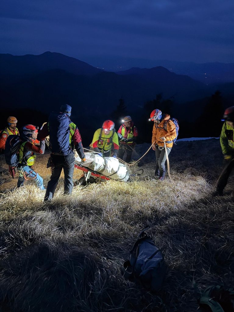 Akcja ratunkowa w g&oacute;rach, ratownicy transportują ofiarę w nocy.
