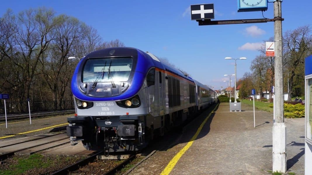 Nowoczesny pociąg na stacji kolejowej w słoneczny dzień, w tle drzewa i niebieskie niebo.