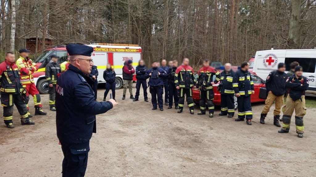 Grupa służb ratunkowych i policjant&oacute;w na miejscu zdarzenia w lesie, w Dobrym Mieście.