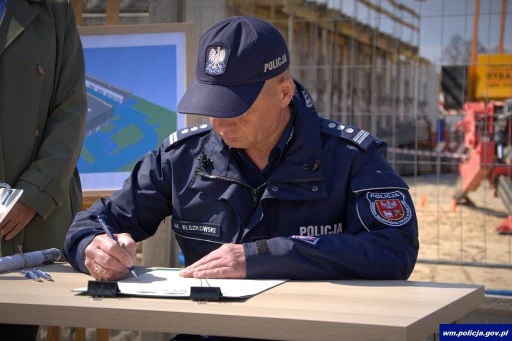 Policjant podpisuje dokumenty przy budowie nowej komendy w Ostr&oacute;dzie, w tle plac budowy.