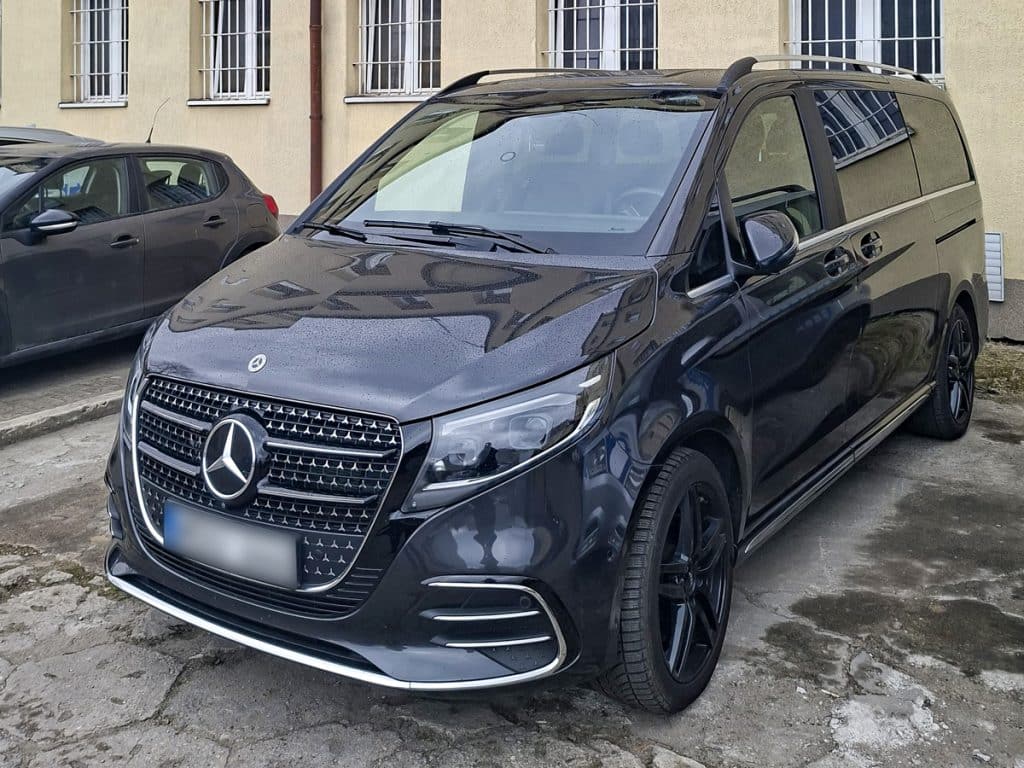 Czarny Mercedes-Benz Vito zaparkowany na parkingu, obok inny samoch&oacute;d, budynek w tle.