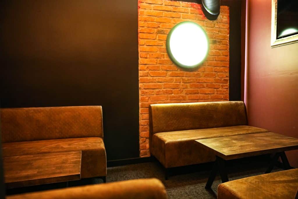 Wnętrze nowego klubu Dyskoteka Music Bar w Olsztynie, z brązowymi kanapami i ceglaną ścianą z oświetleniem.