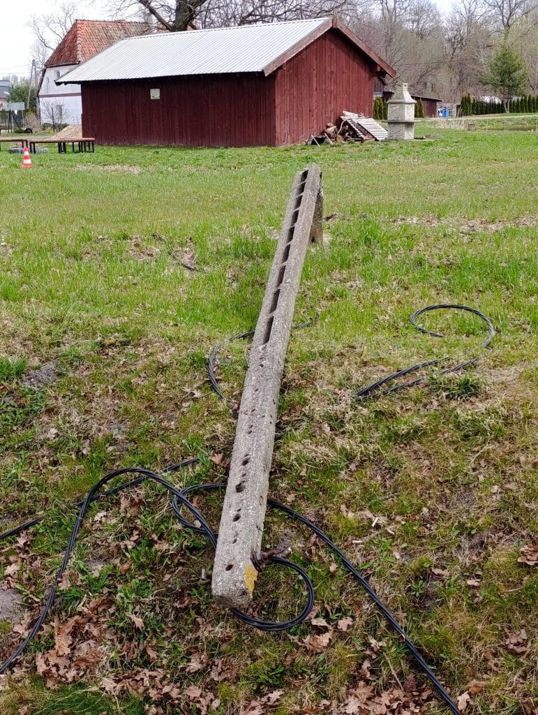Przewr&oacute;cone drzewo na trawniku, uszkodzony słup oświetleniowy i porozrzucone kable.
