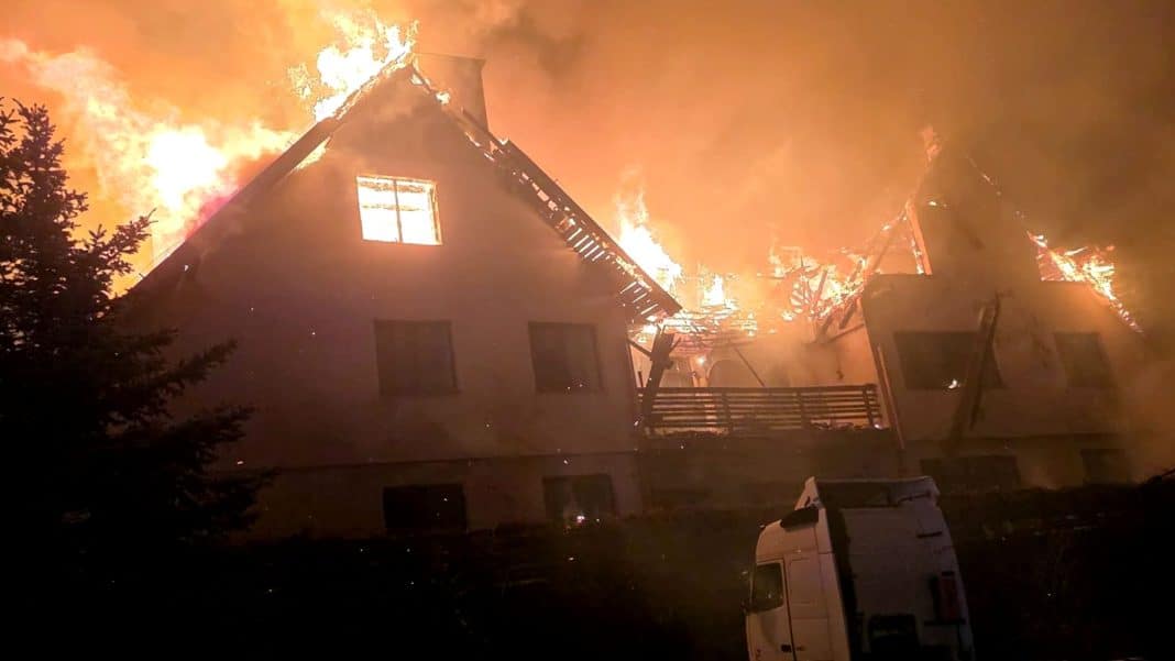 Pożar domu na Mazurach, płomienie i dym unoszą się nad spalonym budynkiem.