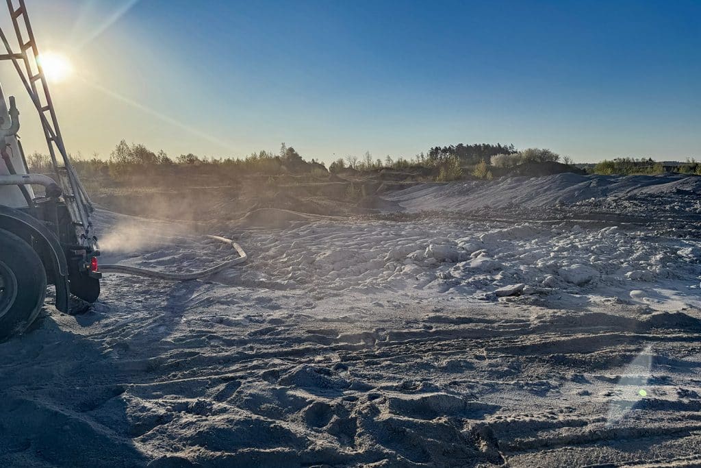 Akcja służb na tle zanieczyszczonego terenu, w tle las i niebo, widoczny sprzęt ratunkowy.