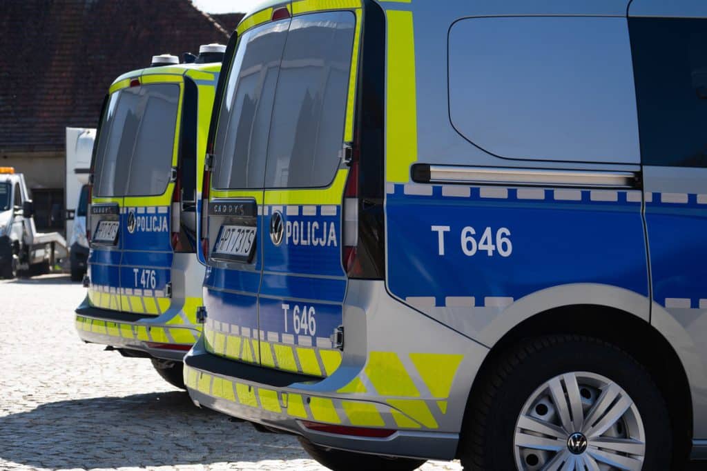 Trzy nowe policyjne radiowozy na parkingu, w policyjnych barwach, z widocznymi oznaczeniami i numerami.