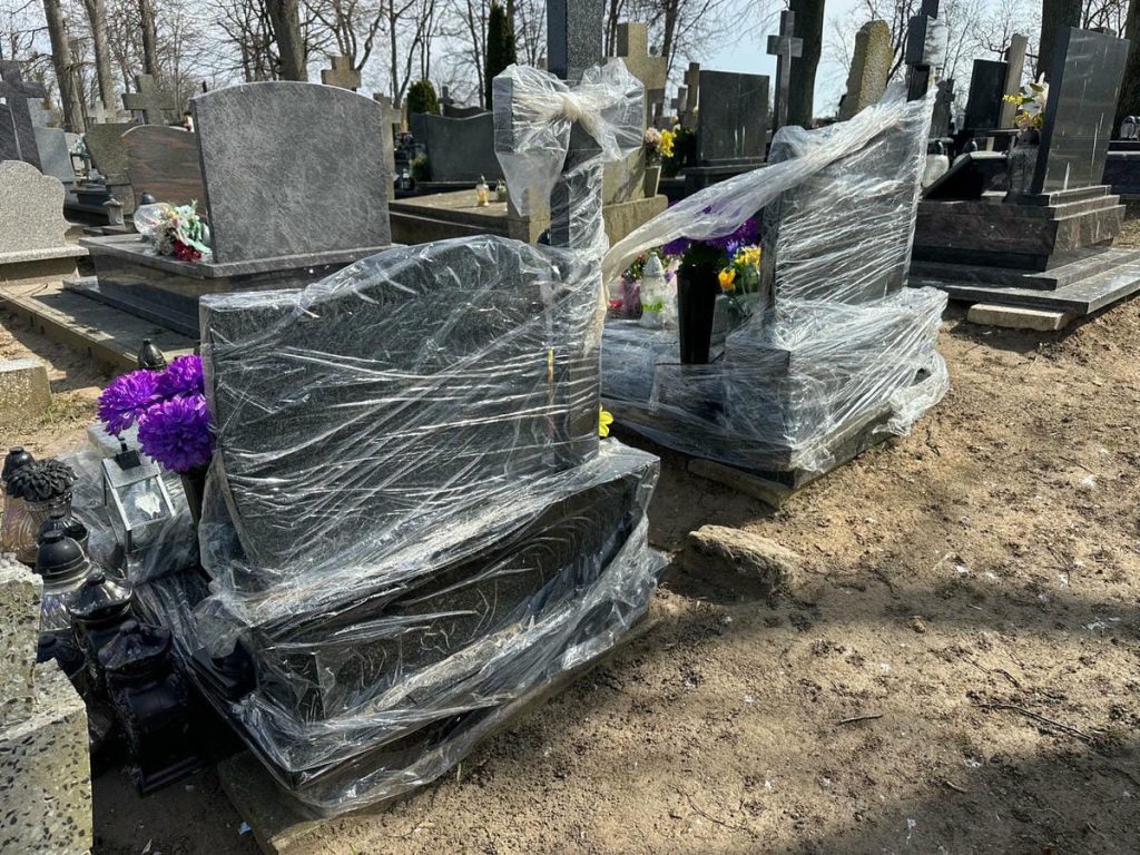 Nagrobki owinięte folią na cmentarzu w Jezioranach, wok&oacute;ł rozrzucone kwiaty i znicze.