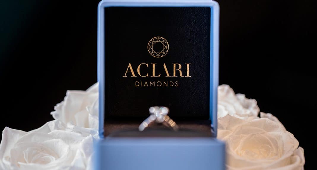 Pierścionek zaręczynowy w elegijnym pudełku na tle białych r&oacute;ż.