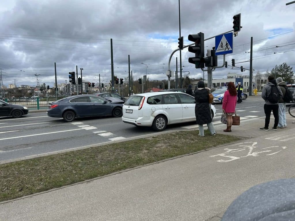 Kolizja dw&oacute;ch samochod&oacute;w na ruchliwym skrzyżowaniu w Olsztynie, na tle sygnalizacji świetlnej i pieszych oczekujących na przejście.