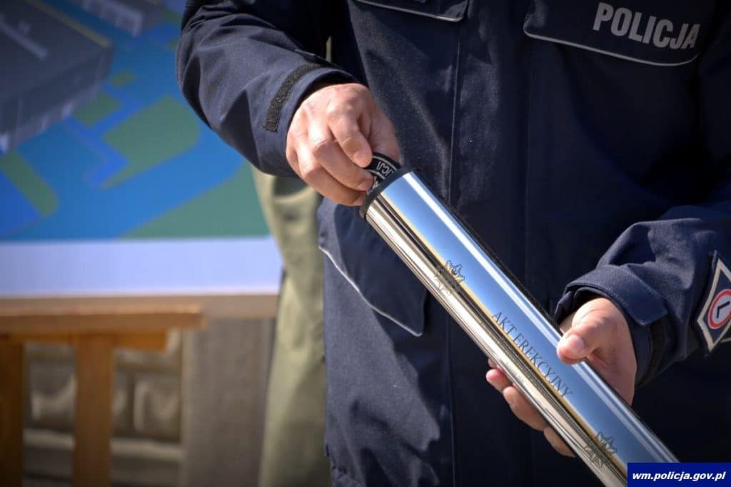 Policjant trzyma akt erekcyjny podczas rozpoczęcia budowy nowej komendy w Ostr&oacute;dzie.