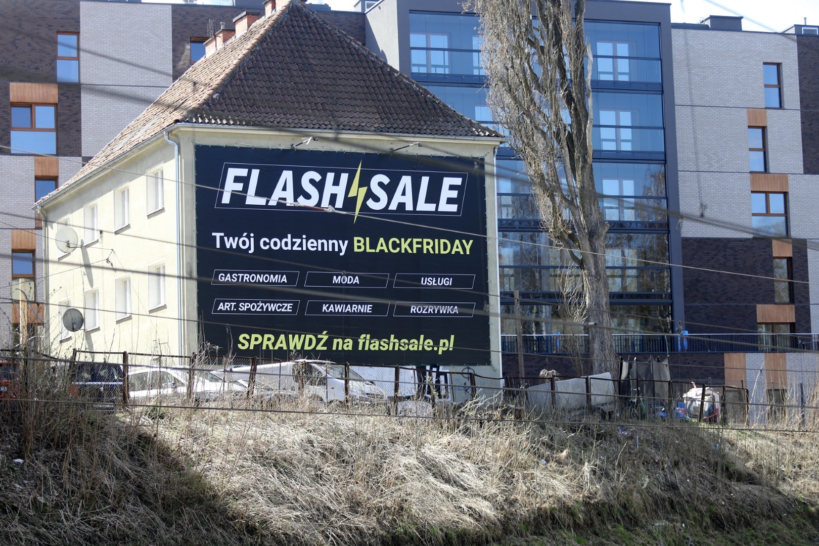 Duży baner reklamowy platformy Flashsale.pl na tle nowoczesnego budynku w Olsztynie.
