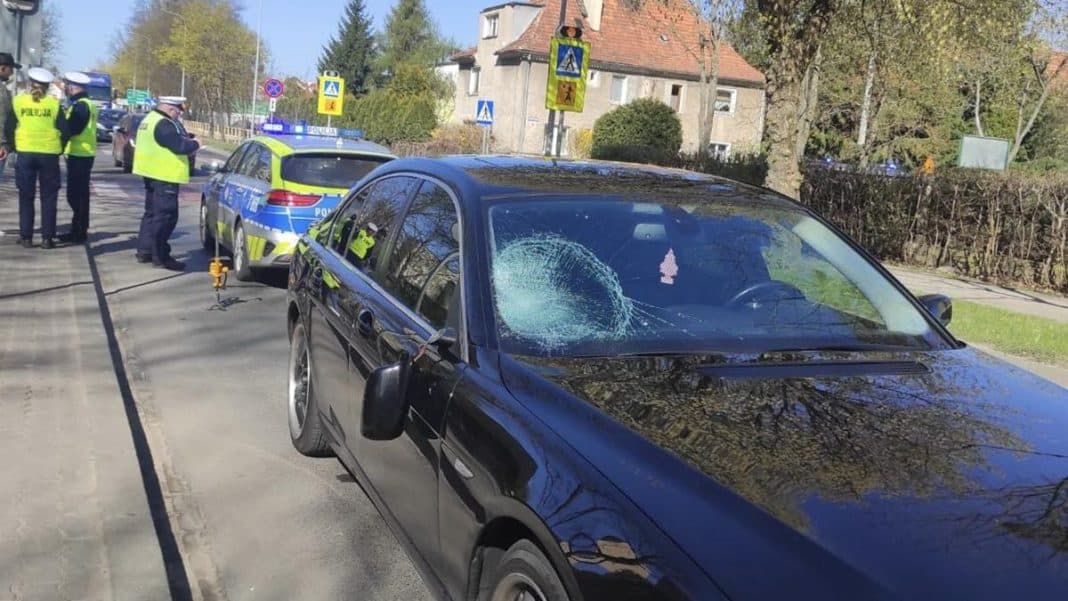 Uszkodzony samoch&oacute;d i policja na miejscu wypadku na przejściu dla pieszych.