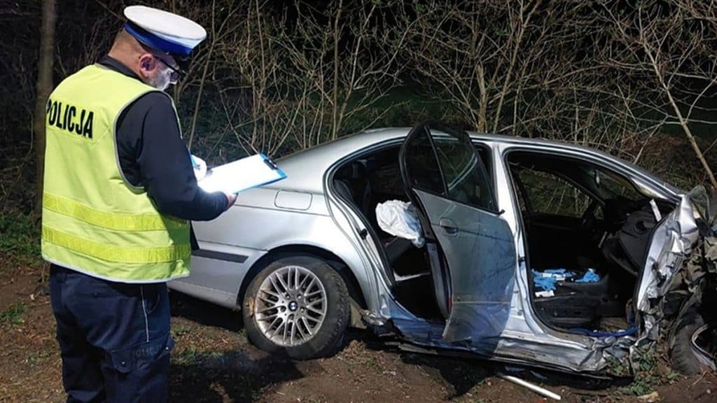 Policjant sporządza notatki przy uszkodzonym samochodzie po wypadku na drodze.