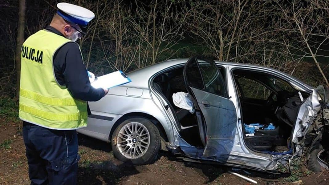 Policjant sporządza notatki przy uszkodzonym samochodzie po wypadku na drodze.