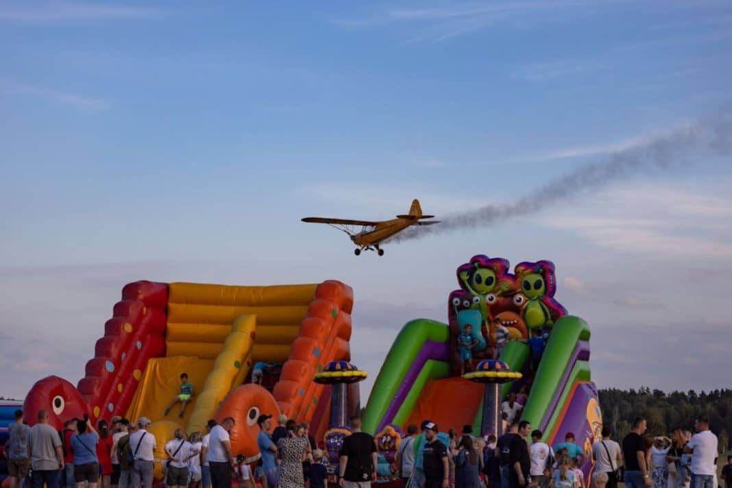 Tłum ludzi na pikniku firmowym z dmuchańcami i samolotem w powietrzu, lato, impreza plenerowa.