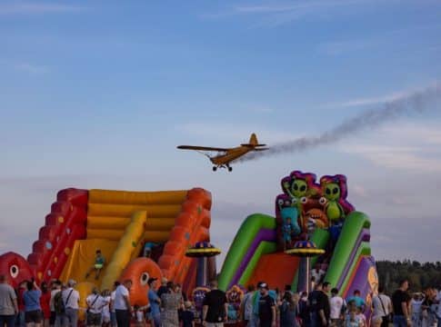 Tłum ludzi na pikniku firmowym z dmuchańcami i samolotem w powietrzu, lato, impreza plenerowa.