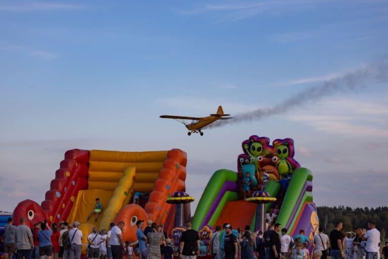 Tłum ludzi na pikniku firmowym z dmuchańcami i samolotem w powietrzu, lato, impreza plenerowa.