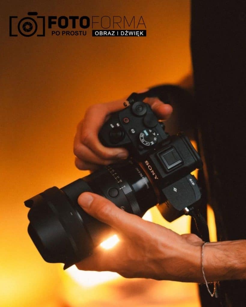 Zdjęcie ręki trzymającej aparat fotograficzny Sony, z ciepłym, rozmytym tłem.