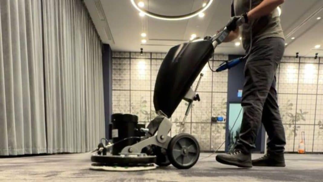 Pracownik czyszczący wykładzinę w nowoczesnym wnętrzu biura lub hotelu.