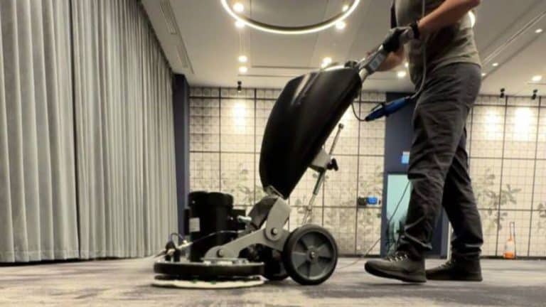 Pracownik czyszczący wykładzinę w nowoczesnym wnętrzu biura lub hotelu.