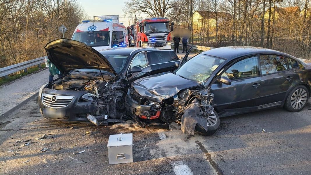 Zderzenie dw&oacute;ch samochod&oacute;w na drodze krajowej, uszkodzone pojazdy i służby ratunkowe na miejscu.